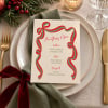 Ribbon Christmas menu on a plate with a sage napkin, gold cutlery and pine sprigs