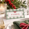 Plaid Christmas placecard on a white festive table with holly, candlelight and a red gingham napkin